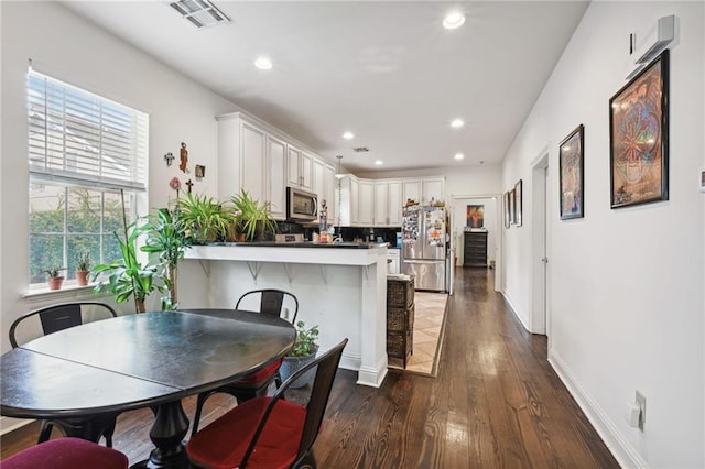 kitchen featuring a kitchen bar, dark wood-type flooring, stainless steel appliances, kitchen peninsula, and white cabinets