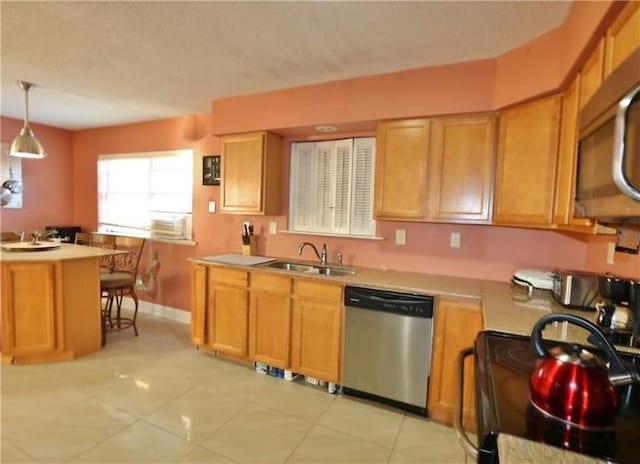 kitchen with sink, kitchen peninsula, appliances with stainless steel finishes, light tile patterned floors, and decorative light fixtures