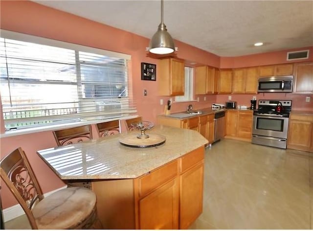 kitchen featuring a center island, sink, hanging light fixtures, stainless steel appliances, and light stone countertops