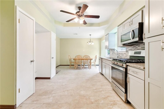 kitchen with ceiling fan with notable chandelier, backsplash, decorative light fixtures, sink, and appliances with stainless steel finishes