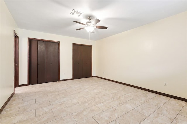 unfurnished bedroom with ceiling fan and multiple closets