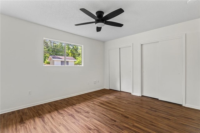 unfurnished bedroom featuring multiple closets, ceiling fan, dark wood-type flooring, and a textured ceiling