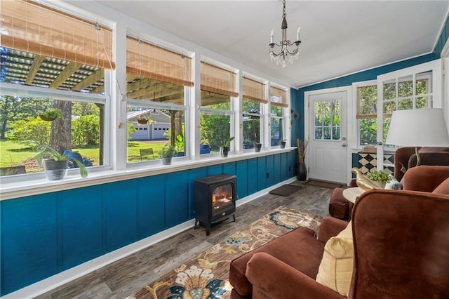 sunroom with a wood stove, an inviting chandelier, and lofted ceiling