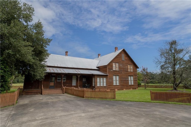 view of front of home with a front yard, fence, covered porch, and metal roof