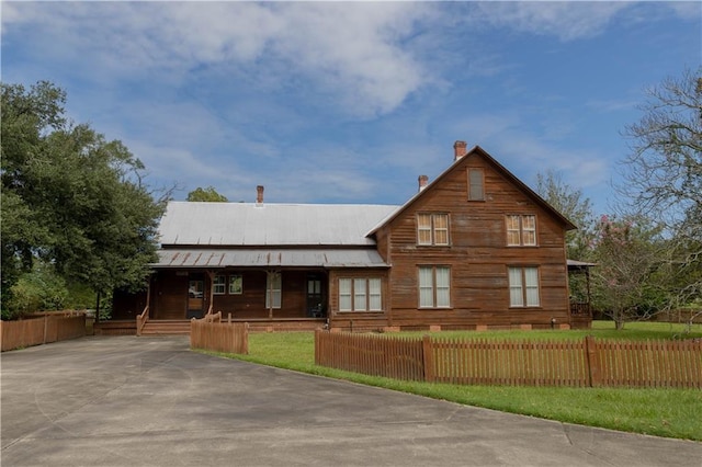 view of front of home featuring a fenced front yard, covered porch, a chimney, and metal roof