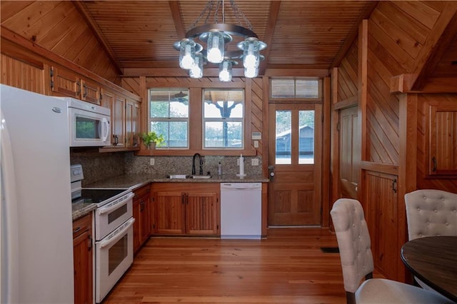 kitchen with white appliances, brown cabinetry, a sink, wood walls, and a notable chandelier