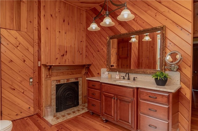 bathroom with a high end fireplace, wooden walls, toilet, wood finished floors, and vanity