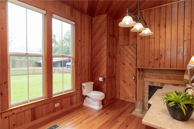 bathroom with wood walls, wood ceiling, toilet, wood finished floors, and plenty of natural light