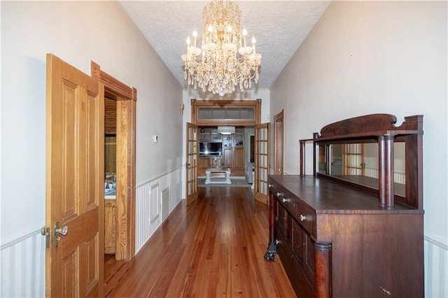 hall with a chandelier, wood finished floors, french doors, and a textured ceiling