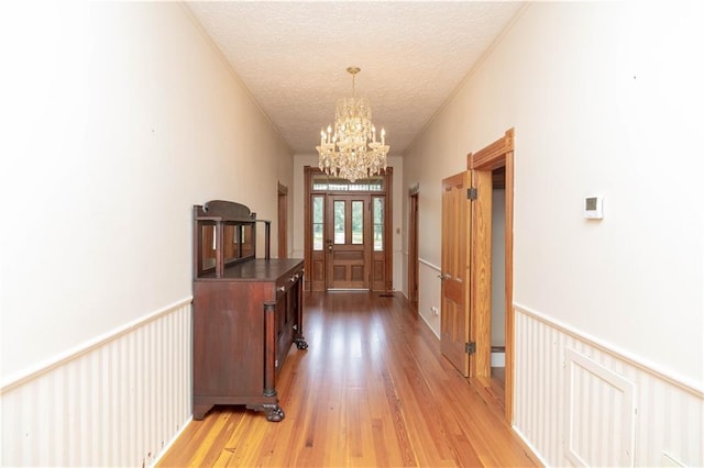 hall featuring a chandelier, a wainscoted wall, light wood finished floors, and a textured ceiling