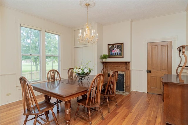 dining area featuring a decorative wall, a fireplace with flush hearth, light wood-style floors, a notable chandelier, and a textured ceiling