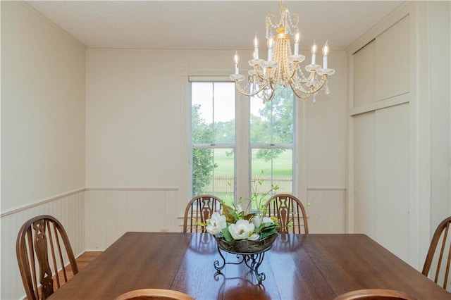 dining area with a textured ceiling, an inviting chandelier, and wainscoting