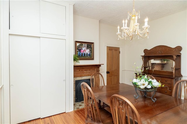 dining room with a textured ceiling, an inviting chandelier, light wood-style flooring, and a fireplace