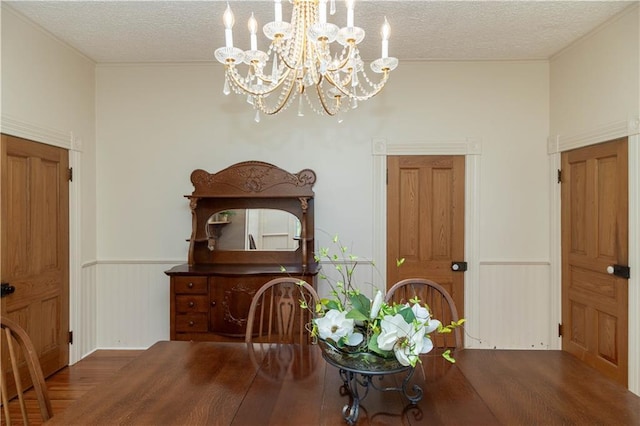 dining room with a wainscoted wall, a textured ceiling, wood finished floors, and ornamental molding