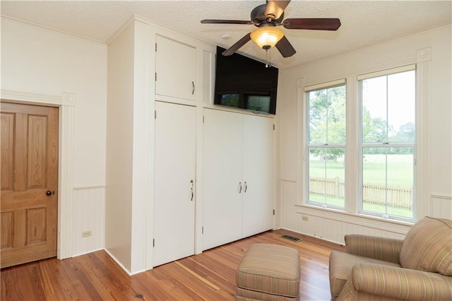 living area featuring visible vents, a textured ceiling, light wood-style floors, and a ceiling fan