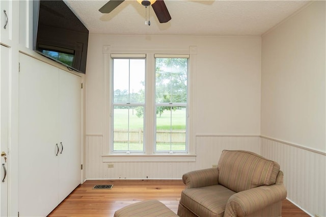 sitting room with a wealth of natural light, a wainscoted wall, a textured ceiling, and light wood-style floors