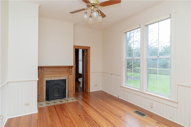 unfurnished living room featuring wood finished floors, a wainscoted wall, visible vents, a fireplace with flush hearth, and a textured ceiling