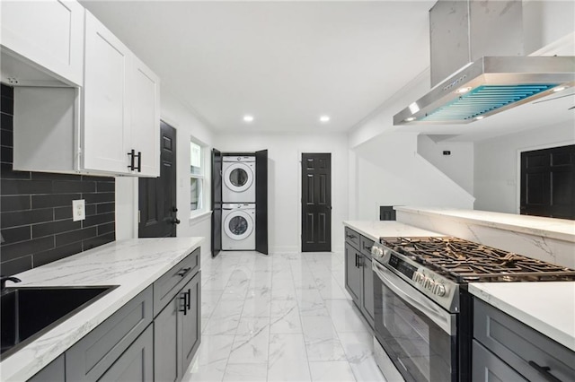 kitchen featuring white cabinets, gray cabinetry, backsplash, stacked washing maching and dryer, and stainless steel gas range