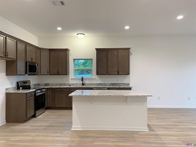 kitchen featuring dark brown cabinetry, light stone counters, a breakfast bar area, a kitchen island, and appliances with stainless steel finishes