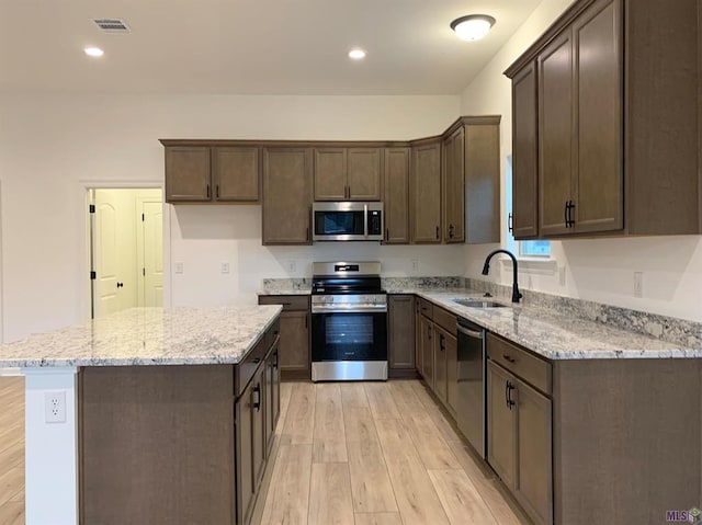 kitchen with appliances with stainless steel finishes, light stone counters, sink, light hardwood / wood-style flooring, and a center island