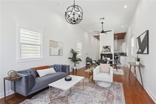 living room with ceiling fan with notable chandelier, hardwood / wood-style flooring, and a towering ceiling