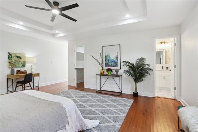 bedroom featuring wood-type flooring, a raised ceiling, connected bathroom, and ceiling fan