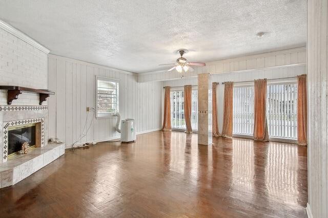 unfurnished living room with ceiling fan, a textured ceiling, wooden walls, dark wood-type flooring, and a fireplace