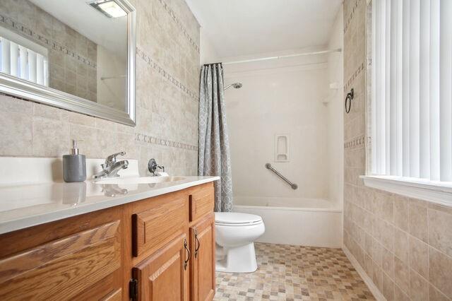 full bathroom with shower / bath combo with shower curtain, tile walls, vanity, and toilet