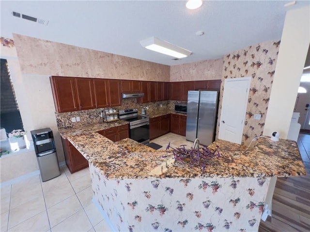 kitchen with stone countertops, backsplash, light tile patterned floors, kitchen peninsula, and stainless steel appliances