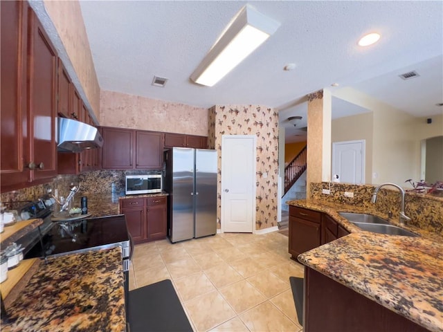 kitchen with sink, light tile patterned floors, appliances with stainless steel finishes, dark stone counters, and decorative backsplash