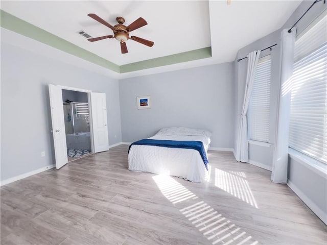 bedroom with ceiling fan, light hardwood / wood-style floors, and a tray ceiling