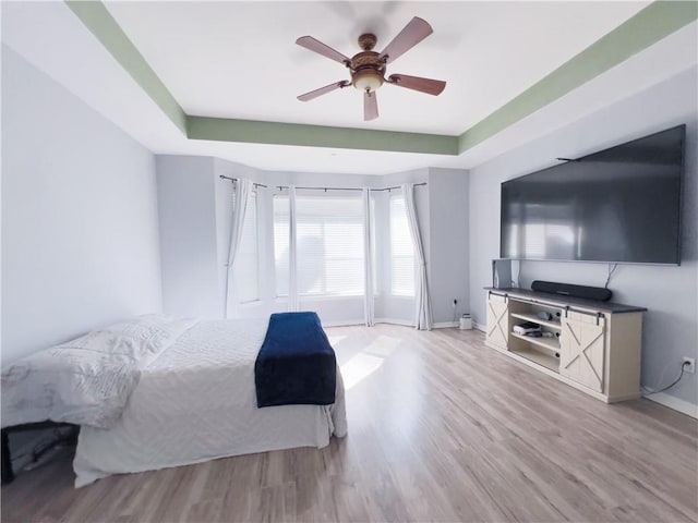 bedroom with a tray ceiling, ceiling fan, and light wood-type flooring