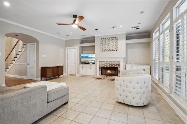 living room featuring ceiling fan, light tile patterned floors, crown molding, and a brick fireplace