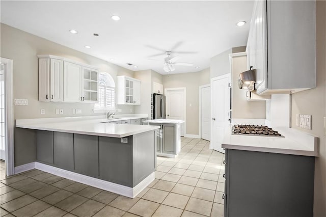 kitchen featuring a peninsula, glass insert cabinets, a ceiling fan, exhaust hood, and appliances with stainless steel finishes
