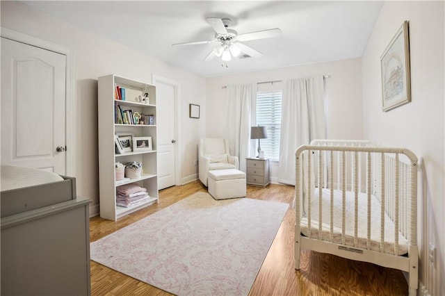 bedroom with light wood-type flooring, a nursery area, and ceiling fan