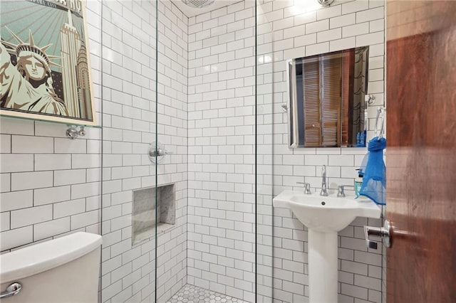 bathroom featuring tile walls, toilet, and a shower with shower door