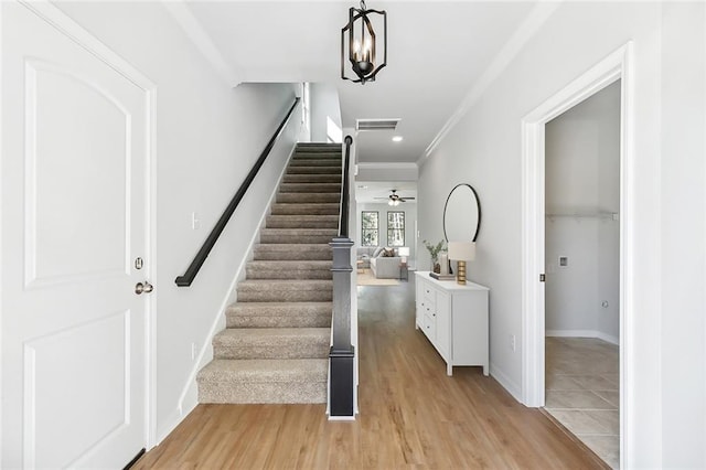 stairway featuring wood-type flooring, ornamental molding, and ceiling fan with notable chandelier