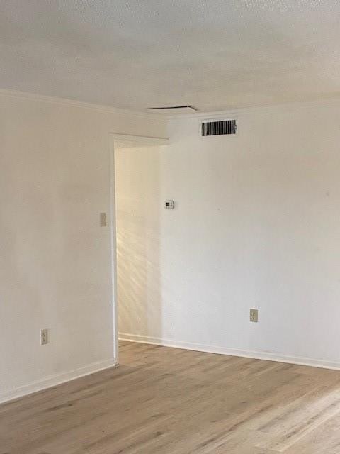 empty room with a textured ceiling, ornamental molding, and hardwood / wood-style floors