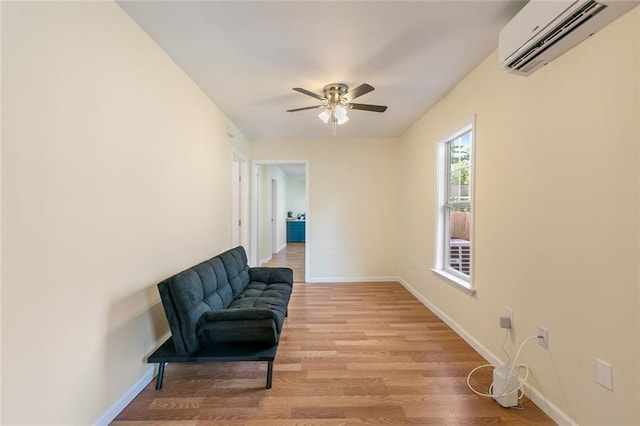 sitting room featuring a wall mounted air conditioner, light wood-type flooring, and ceiling fan