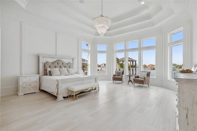 bedroom with a raised ceiling, a towering ceiling, a chandelier, and light hardwood / wood-style flooring