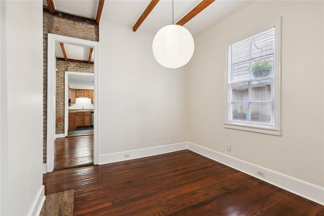 spare room with brick wall, dark hardwood / wood-style floors, and beam ceiling