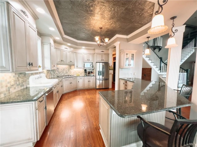 kitchen with white cabinetry, hanging light fixtures, stainless steel appliances, light hardwood / wood-style flooring, and dark stone countertops