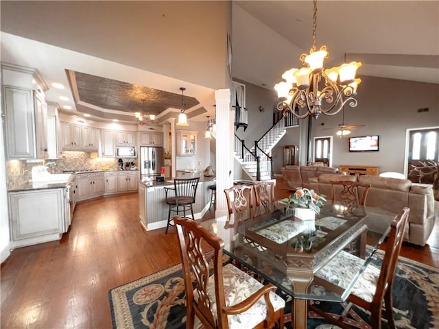 dining area with hardwood / wood-style floors, ceiling fan with notable chandelier, high vaulted ceiling, and a tray ceiling