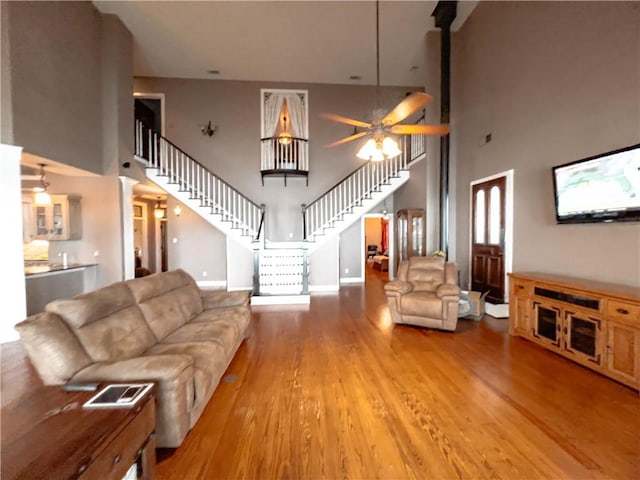 living room with ceiling fan, light wood-type flooring, and a towering ceiling