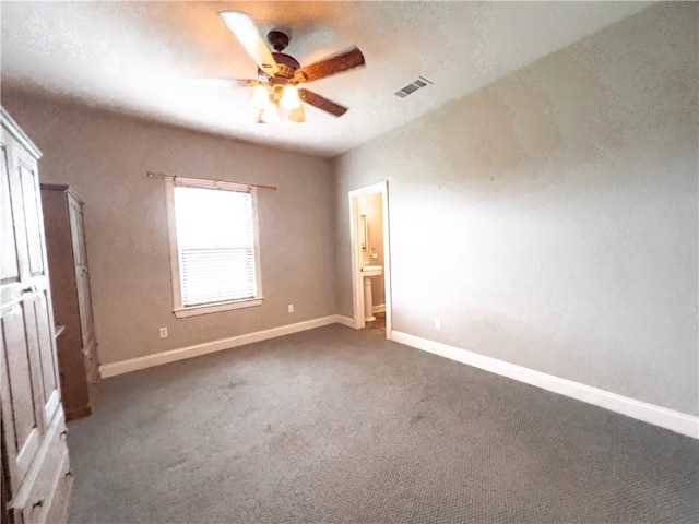 unfurnished bedroom with dark colored carpet, ensuite bath, and ceiling fan