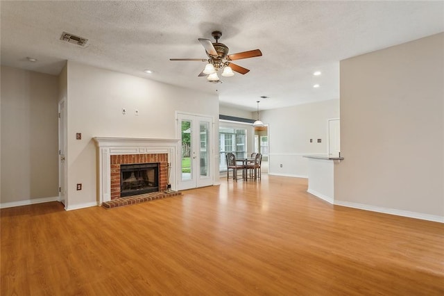 unfurnished living room with a textured ceiling, a brick fireplace, ceiling fan, and light hardwood / wood-style floors