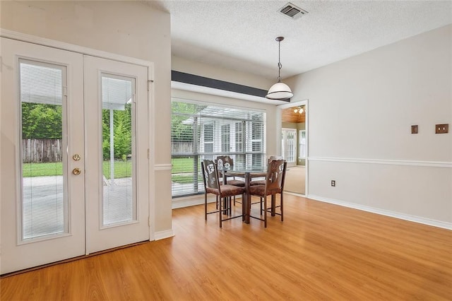 dining room featuring a textured ceiling, light hardwood / wood-style flooring, and french doors