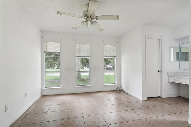 tiled empty room with ceiling fan, a textured ceiling, and a healthy amount of sunlight