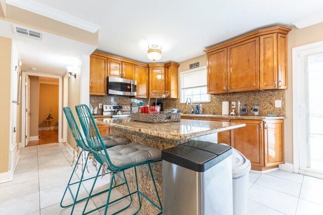 kitchen with appliances with stainless steel finishes, light stone counters, a kitchen island, and backsplash