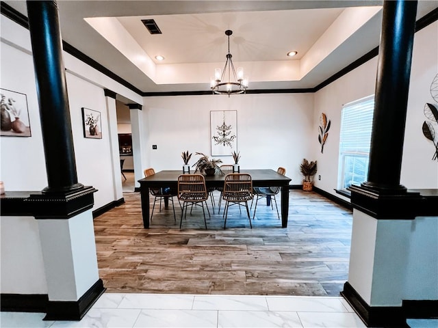 dining space with an inviting chandelier, decorative columns, a tray ceiling, and wood-type flooring